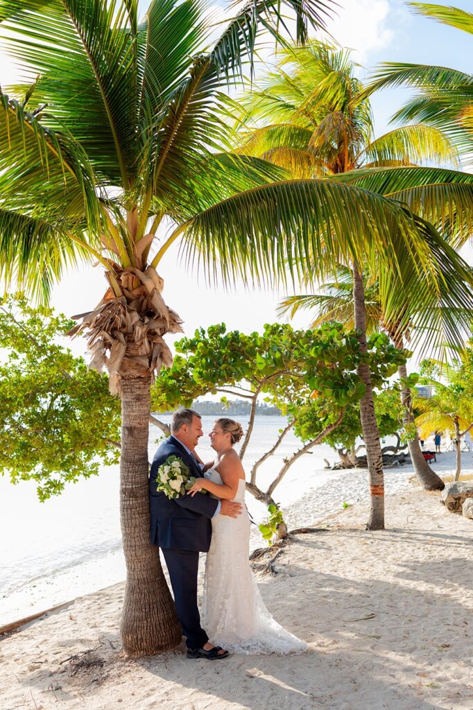 Bride and groom embracing under palm trees on an Aruba beach